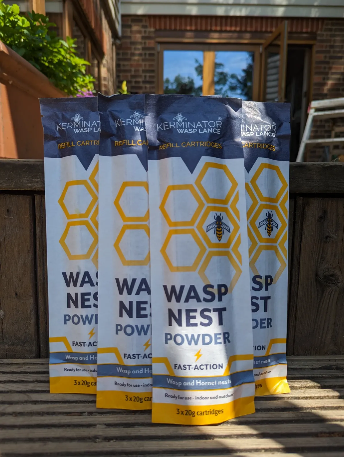 Four packages of Kerminator Wasp Nest Powder on a wooden surface with a garden background.