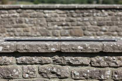 Long thin carbon fibre tube resting on a stone wall