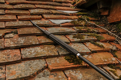 Rust-colored roof tiles with a Kerminator end tube inserted underneath them, roof showing signs of wear and moss growth.