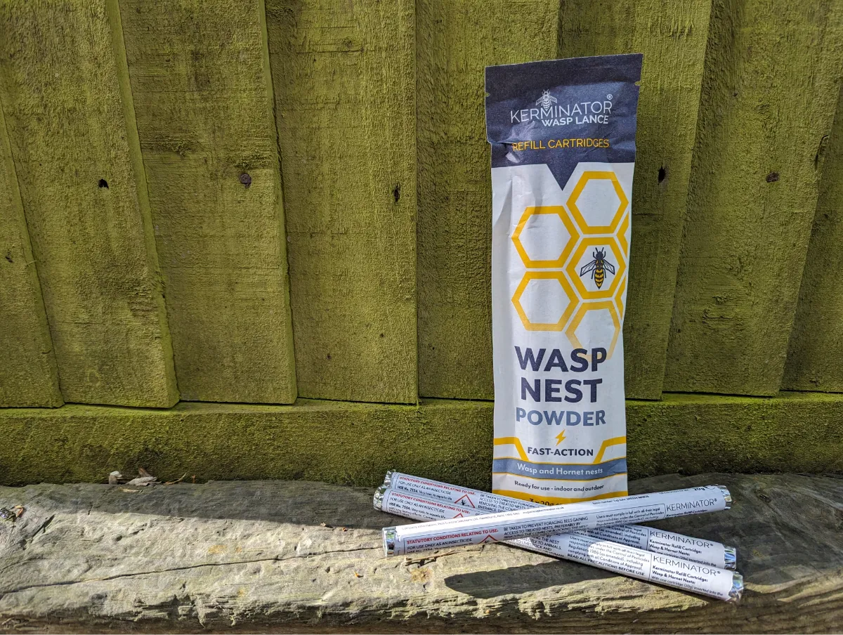 Kerminator wasp nest powder packaging on a wooden surface with a wooden fence background